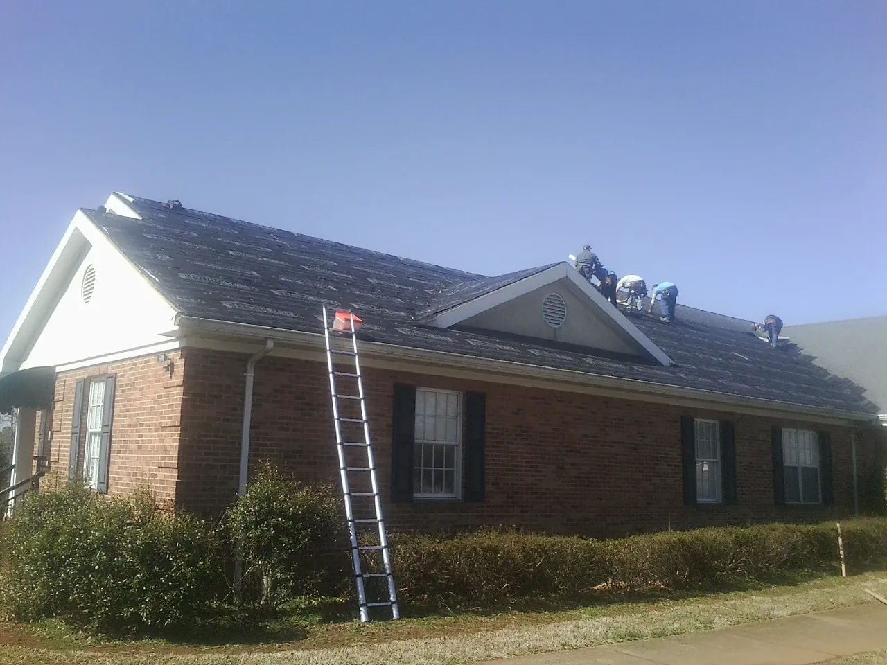 Crew tearing shingles off a brick ranch roof with a ladder set — Emergency Roof Repair work by our crew in Westernville