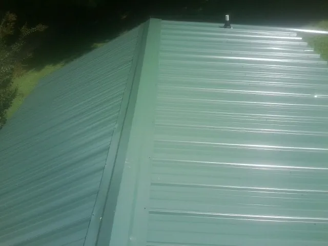 New green metal panels meeting at the ridge of a roof — Flat Roof Repair work by our crew in Westernville