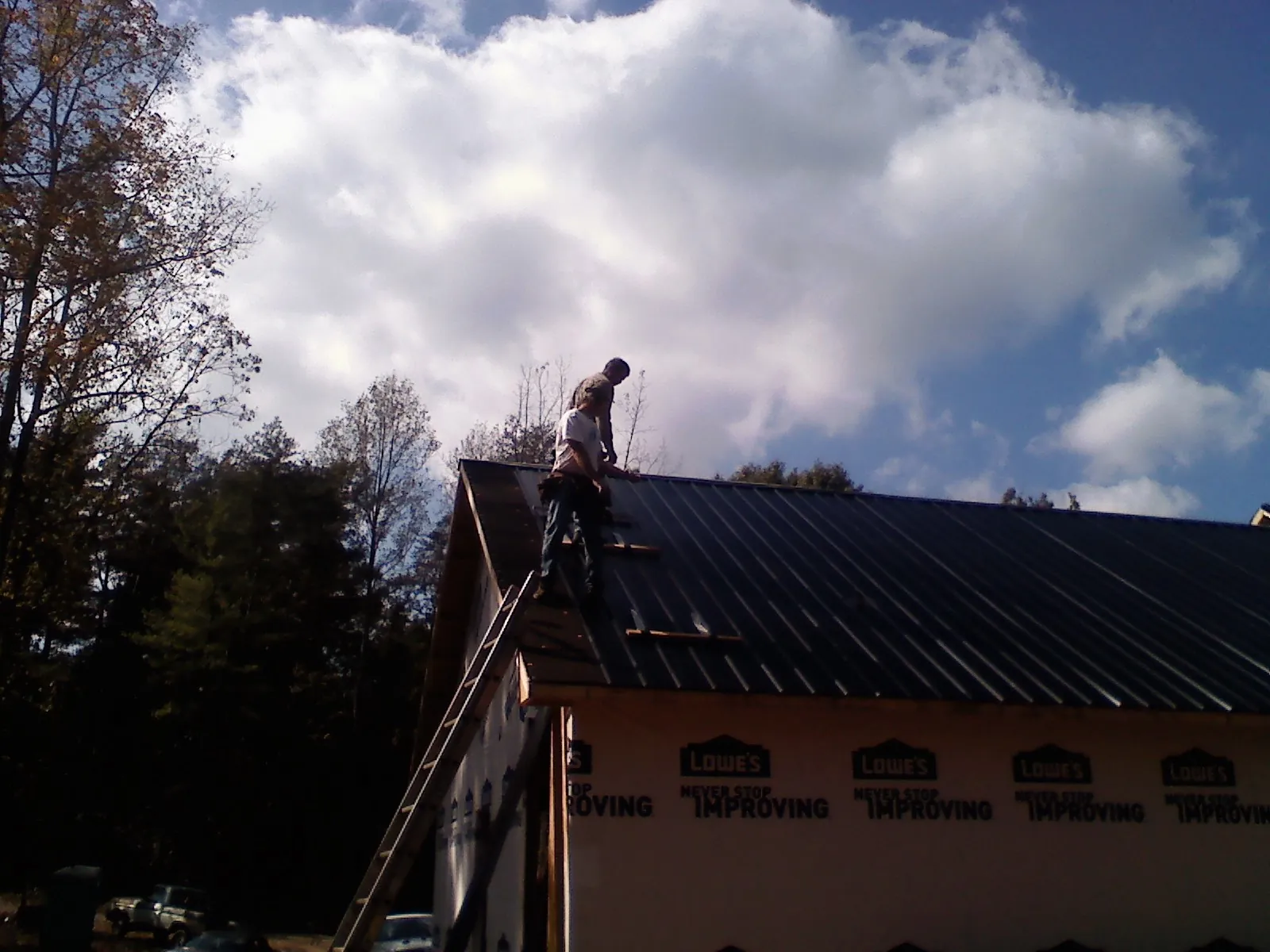 Roofer fastening dark metal panels high against a cloudy sky, from a Roof Inspection job in Westernville