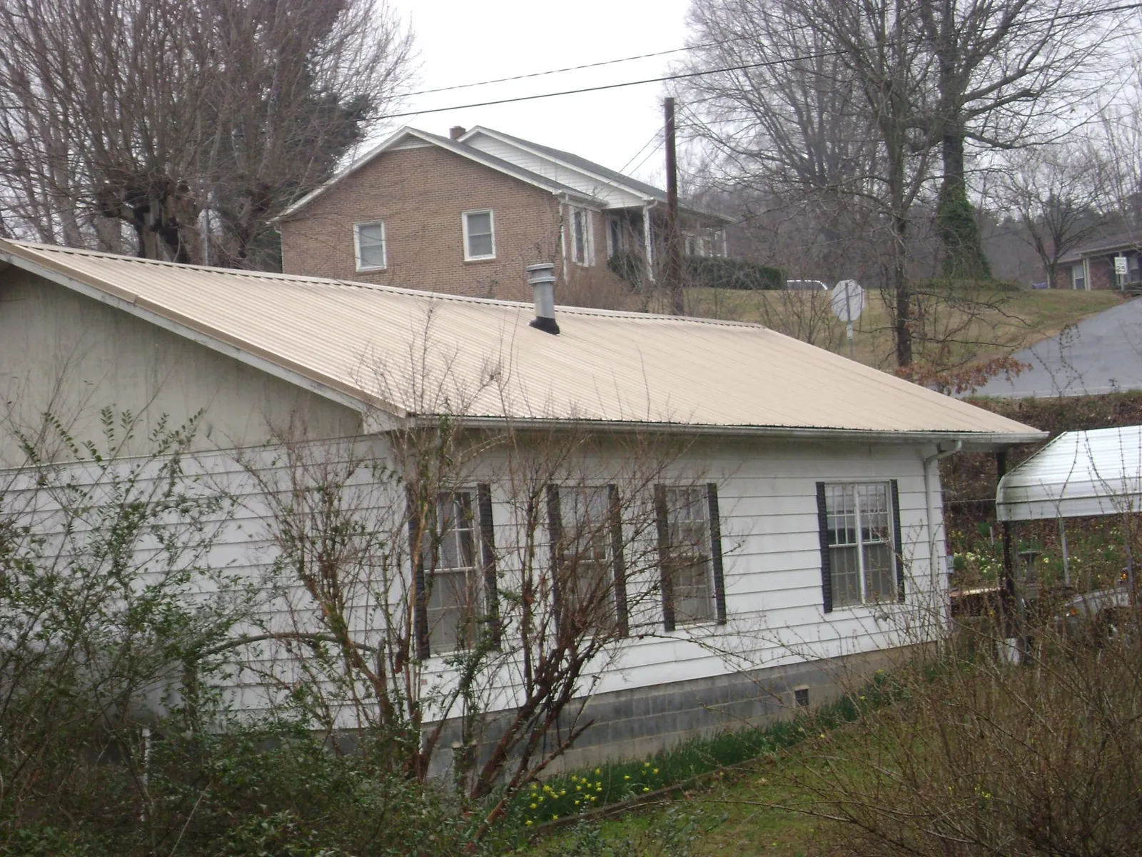 Tan metal roof on a white sided house set into a hillside — Commercial Roofing by Roofing Brothers in Westernville